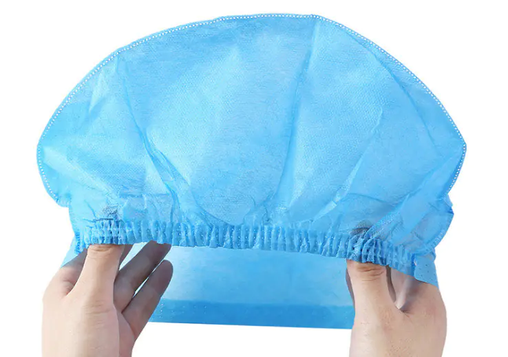 Hands holding a blue disposable hair cap.