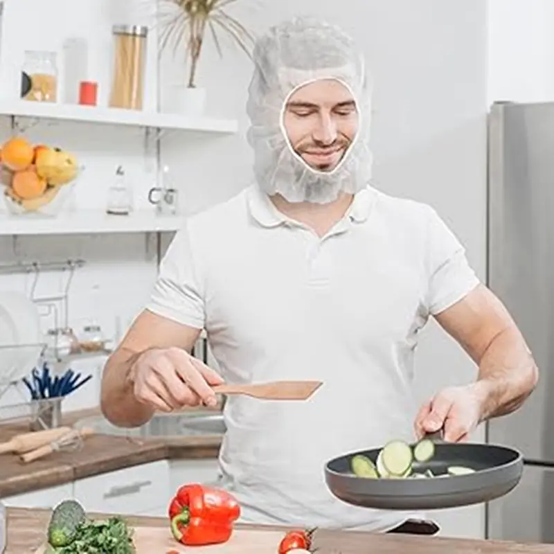 Man cooking vegetables wearing hair net in kitchen.