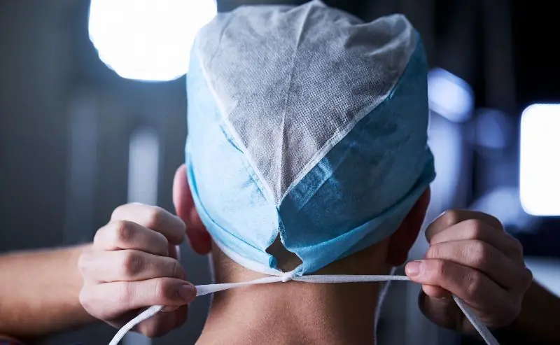 Surgeon tying surgical cap straps before operation.