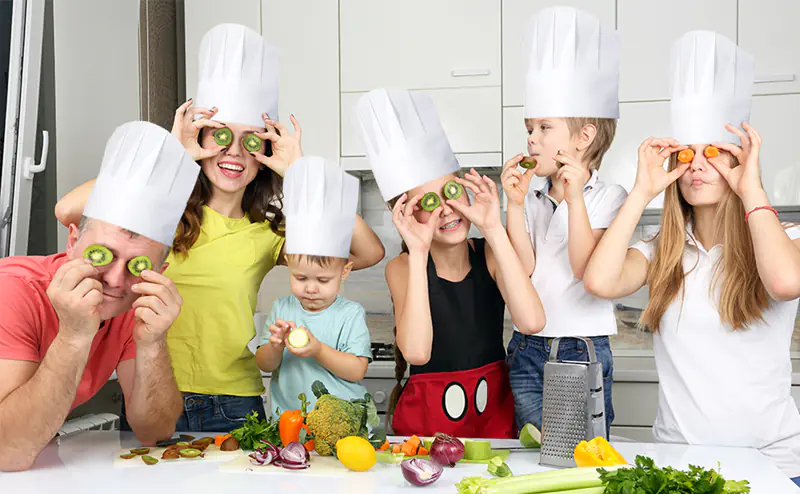 Family cooking fun with chef hats, vegetables in kitchen.