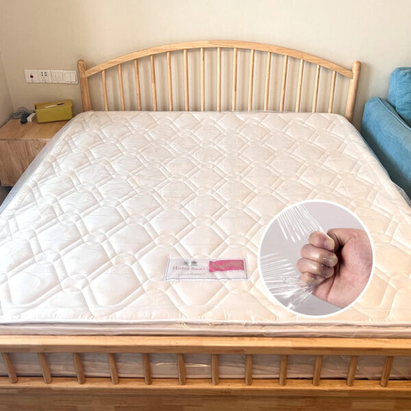 Wooden bed with white mattress and plastic cover.