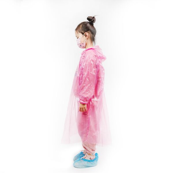 Child in pink raincoat and mask standing sideways.