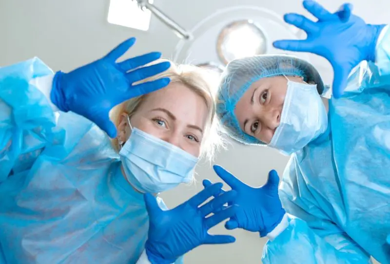 Smiling surgeons in gloves and masks waving.