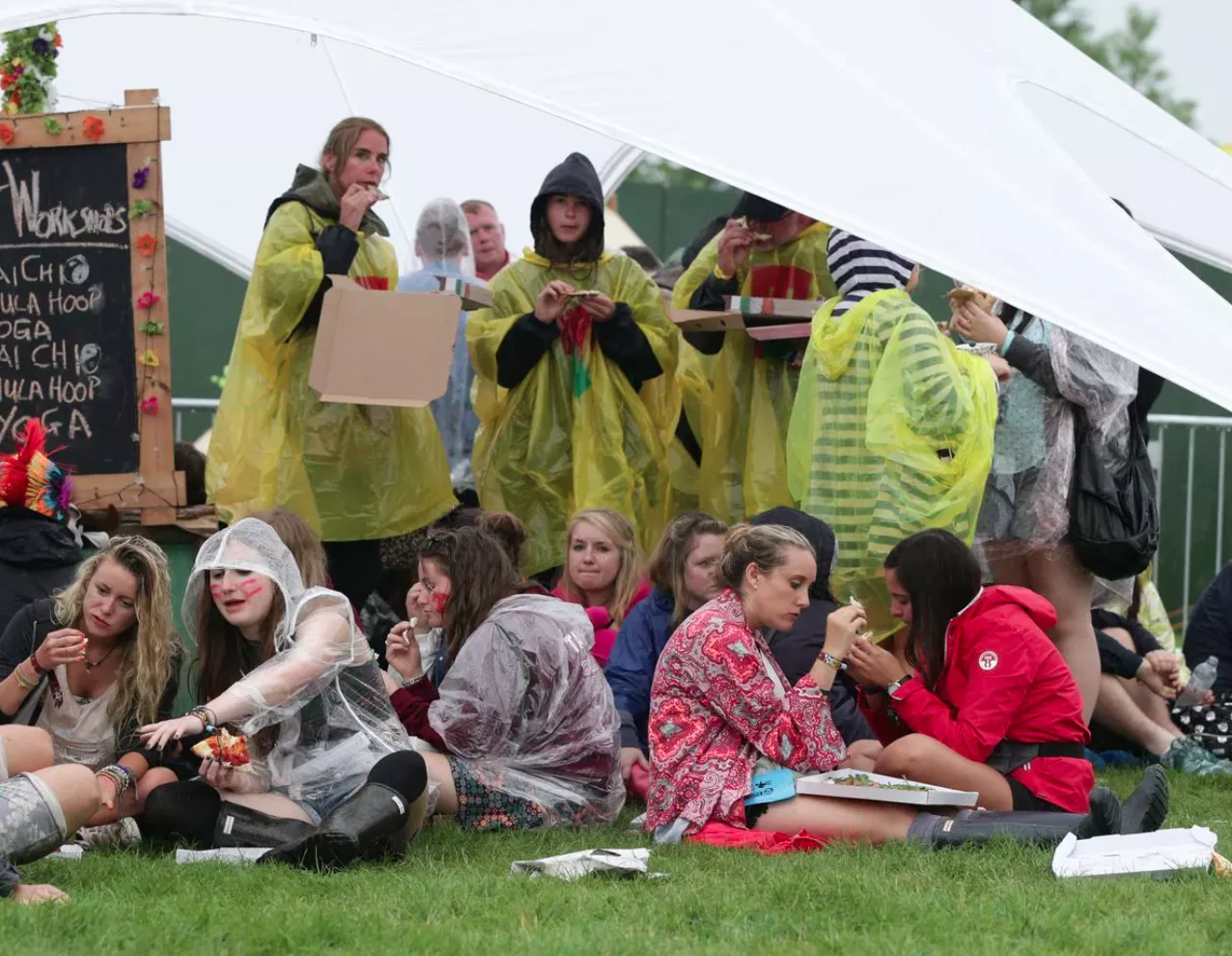 Festival-goers eating under a tent in rain ponchos.